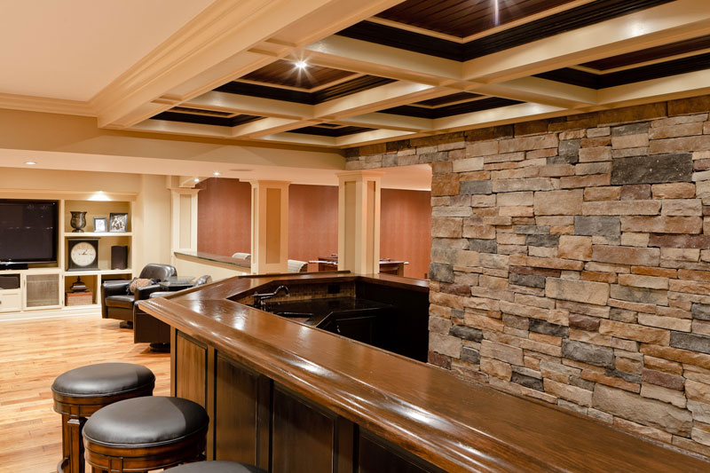 Basement wet bar with stone wall behind it. Entertainment center to the side.