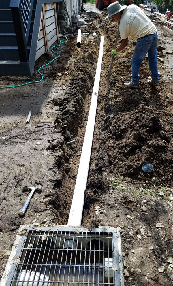Man digging drainage ditch with PVC pipe and junction box.